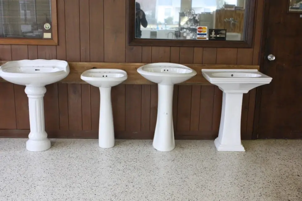 Four white pedestal sinks against wood panelling in the Ellsworth Plumbing & Heating showroom